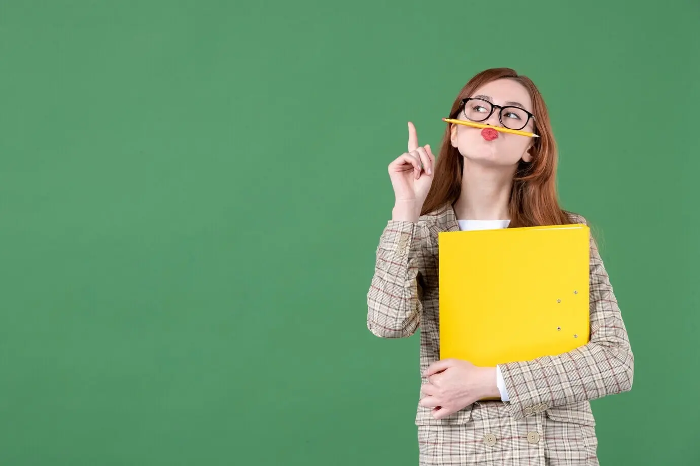 Porträt einer Lehrerin mit einer Mappe und einem Bleistift um ihren Mund vor grünem Hintergrund.