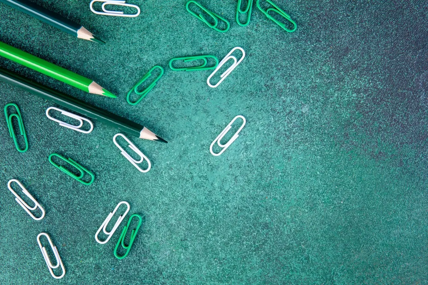 Draufsicht mit Platz für Text: grüne Bleistifte mit grünen und weißen Büroklammern auf grünem Hintergrund.